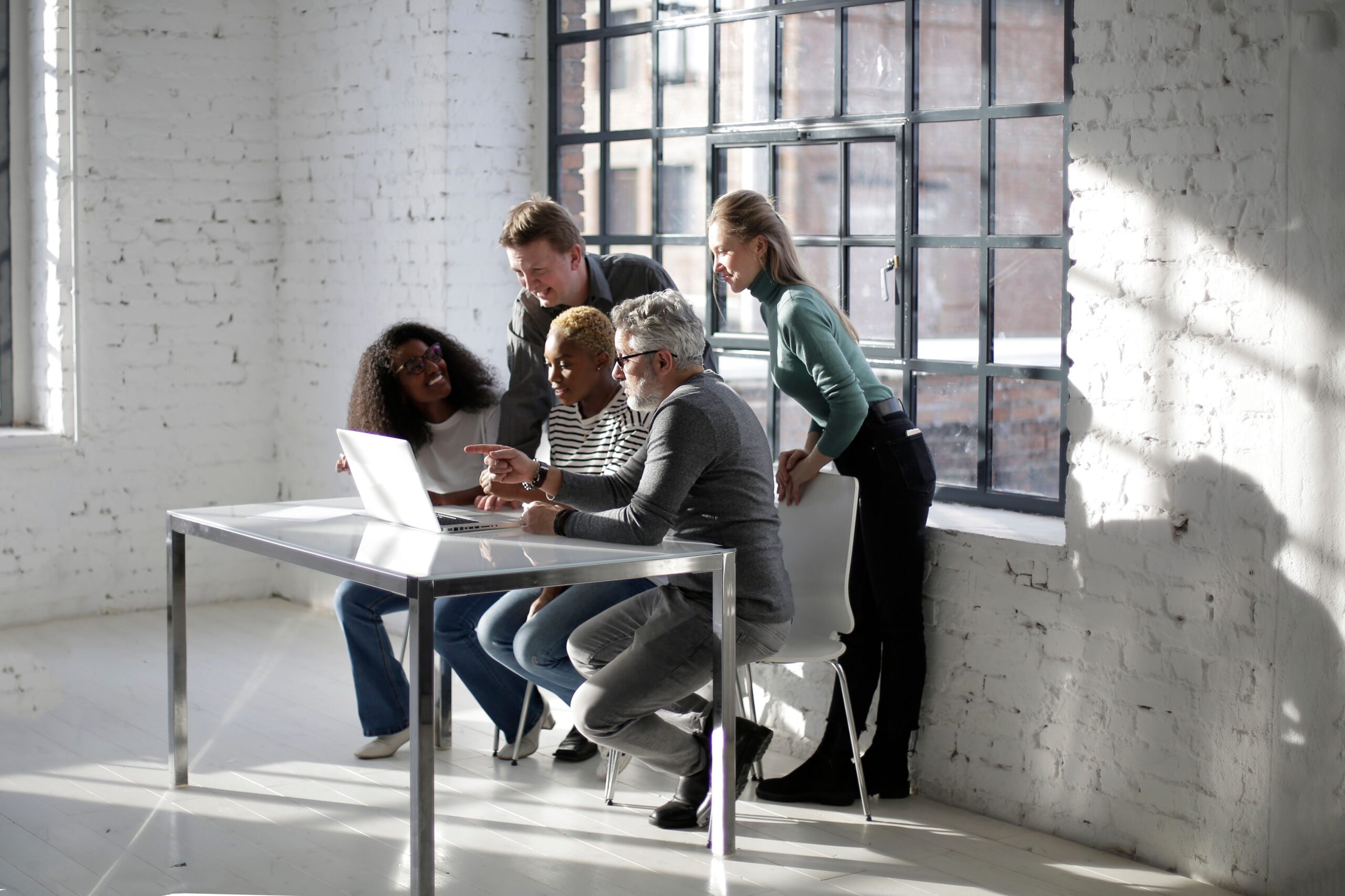 Group of multiracial coworkers of different age in casual outfit gathering at table with netbook and working on business project